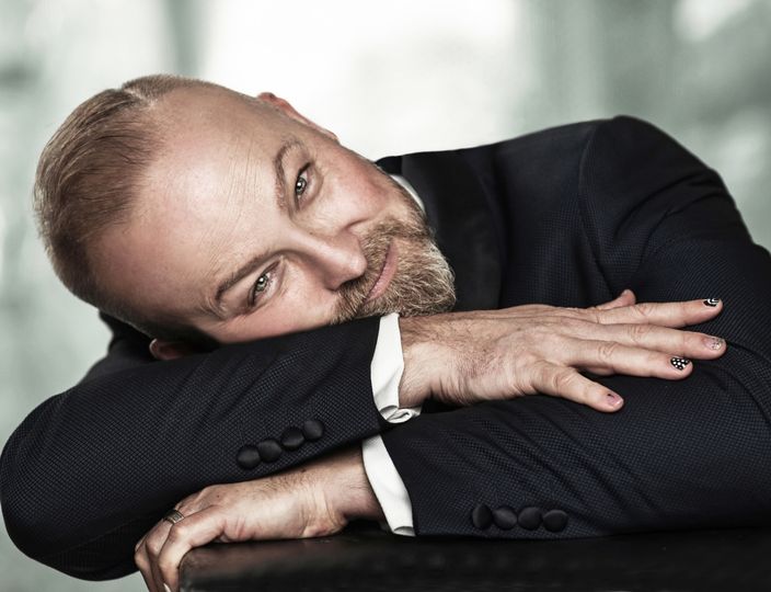 Michael Bach photographed in a contemplative close-up: shaved head, salt-and-pepper beard, hand resting near the chin.