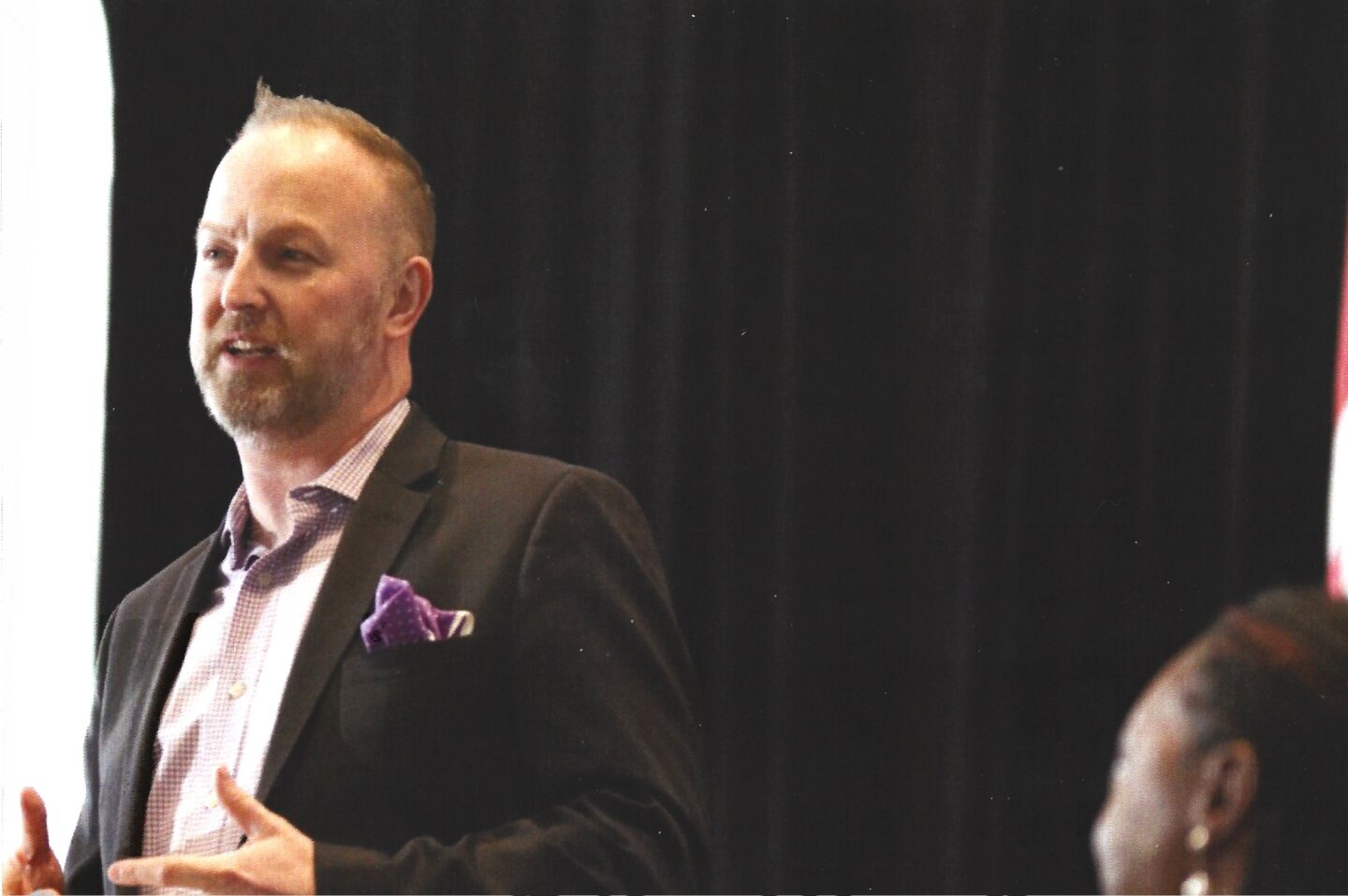 Michael Bach speaking onstage, close-up